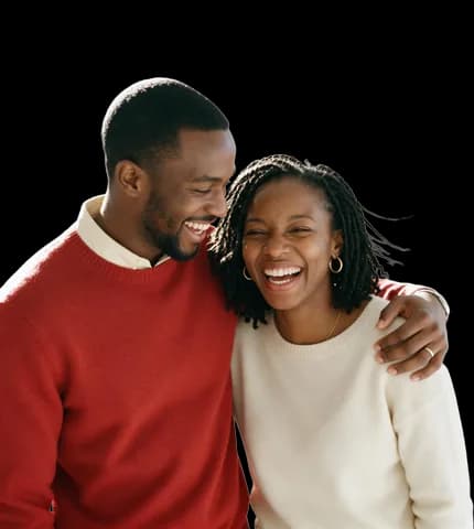 A young couple laughing together, his arm around her shoulder