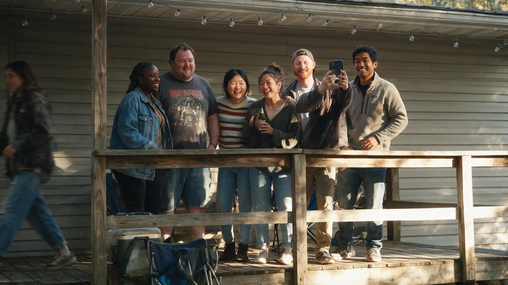 Six friends in their thirties crowded on the porch of a rented house in the afternoon, one holding up a phone